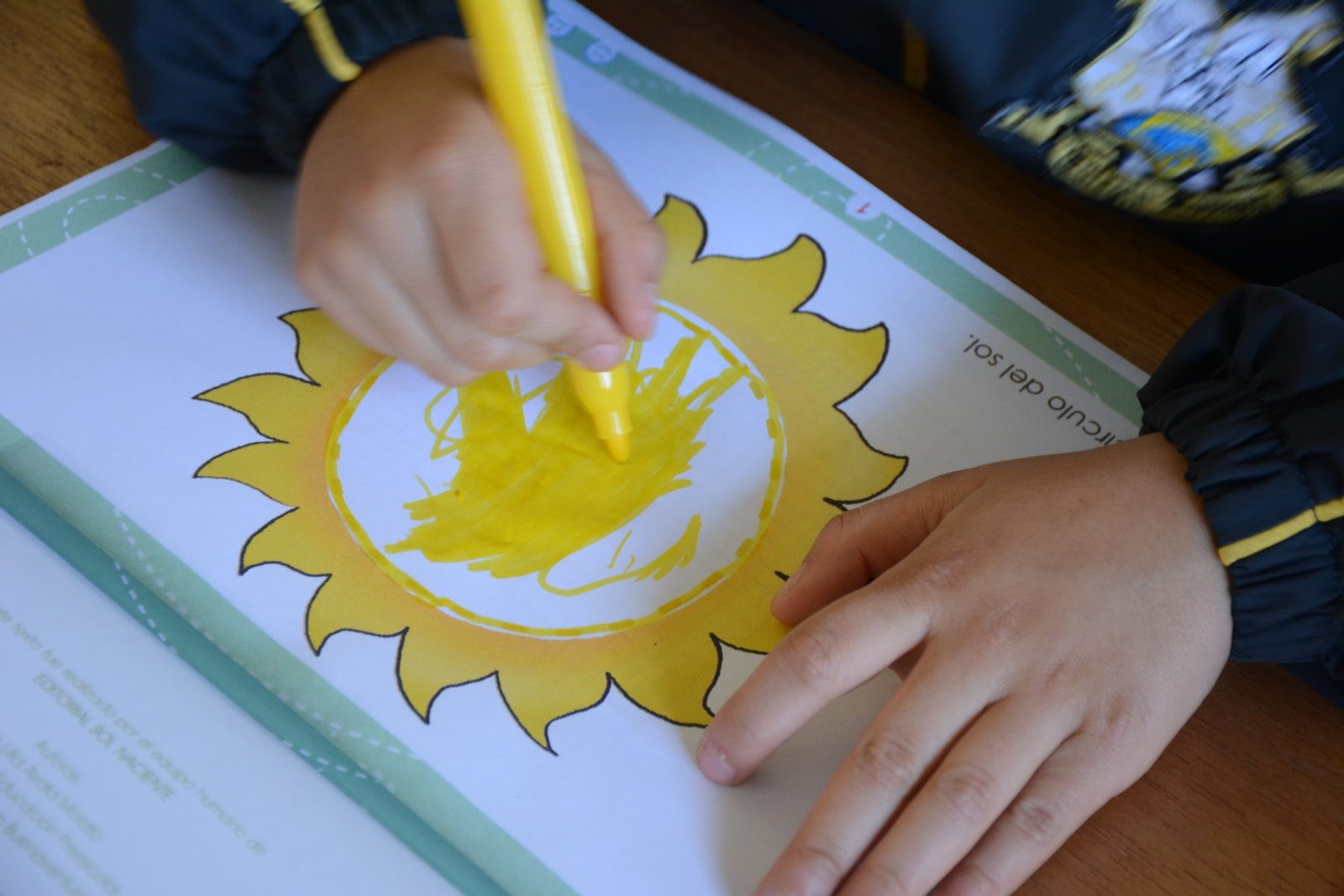 Un niño colorea el sol en una cartilla de Editorial Sol Naciente